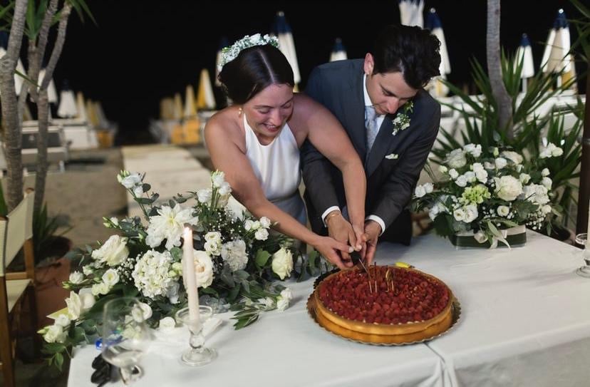 una coppia di sposi taglia una torta su un tavolo decorato sulla spiaggia